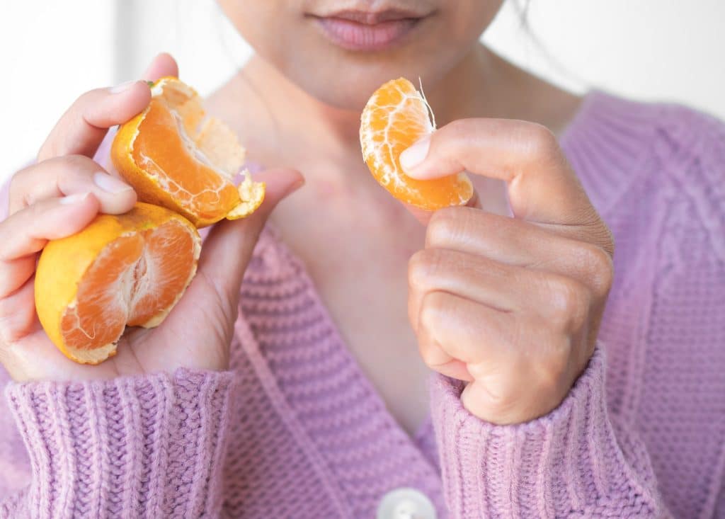 Woman with sweater holding orange for eat.